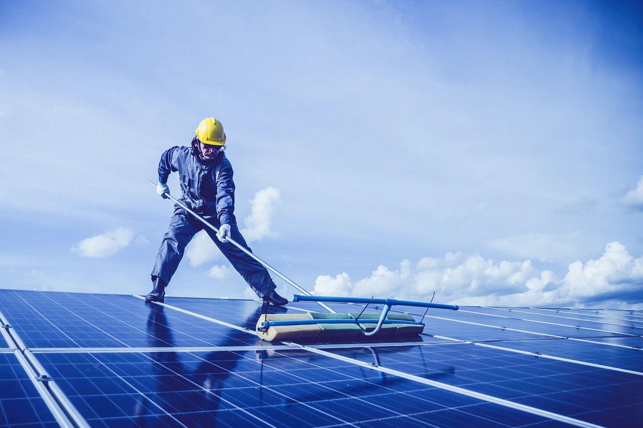 Man cleaning solar panel on roof with a mop